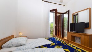 Un dormitorio con dos camas, un televisor sobre un mueble de madera y una puerta al balcón.
