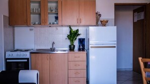 A compact kitchen with wooden cabinets, a stove, a sink, and a refrigerator. - Apartments Jasko (Rab)