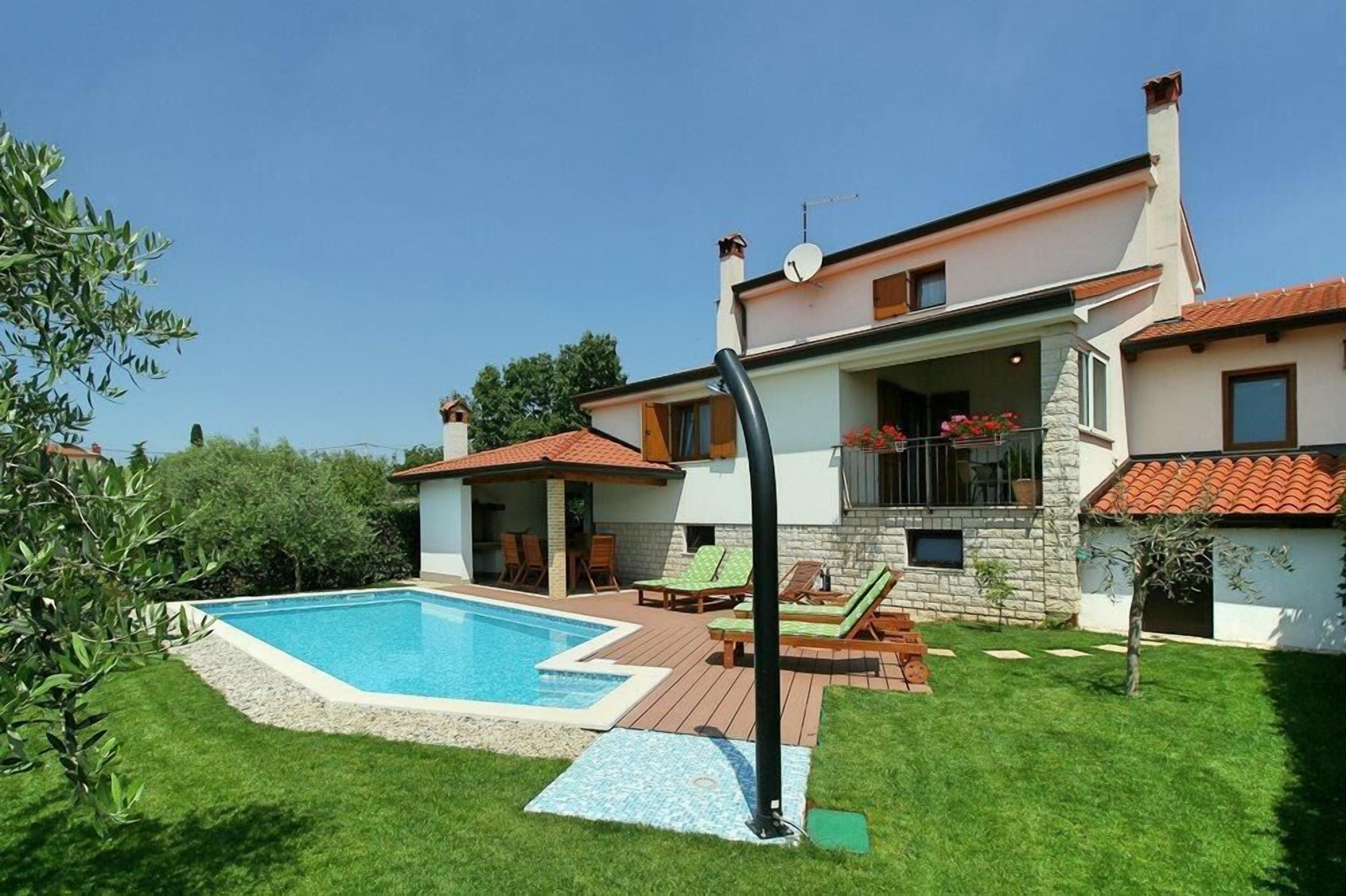 A two-story house with a swimming pool, outdoor furniture, and a stone facade.