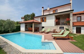 Une maison à deux étages avec une piscine, un espace salon extérieur et un balcon.