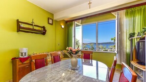 A dining area with a round table, chairs, a vase with flowers, a coffee maker, and a view of the outdoors through large windows. - Holiday House Anica (Bibinje)