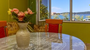 A round table with a patterned tablecloth, a textured vase with flowers, and a view of a body of water through a window. - Holiday House Anica (Bibinje)