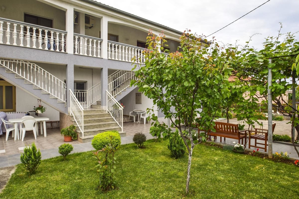 A two-story building with a balcony, a staircase, and a well-maintained garden with a bench and potted plants.