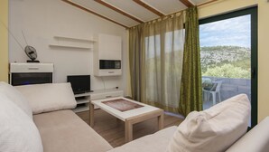 Ein modernes Wohnzimmer mit einer Couch, einem Couchtisch, einem Fernseher und einem Balkon mit Blick auf die Landschaft.