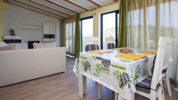 Ein modernes Wohnzimmer mit Essbereich, Holzbalkendecke, einer Couch, einem Fernseher und einem Tisch mit Tischdecke im Naturdesign.