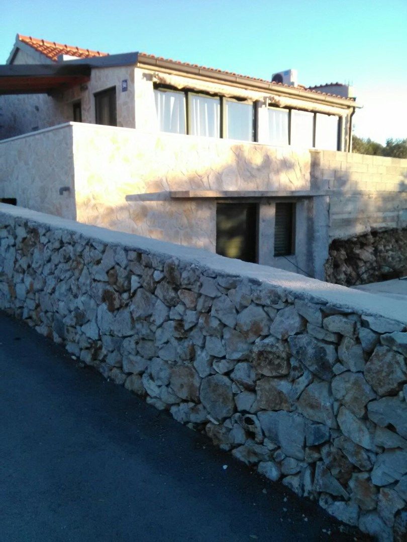 A modern building with a stone wall in front, a flat roof, and a clear sky.