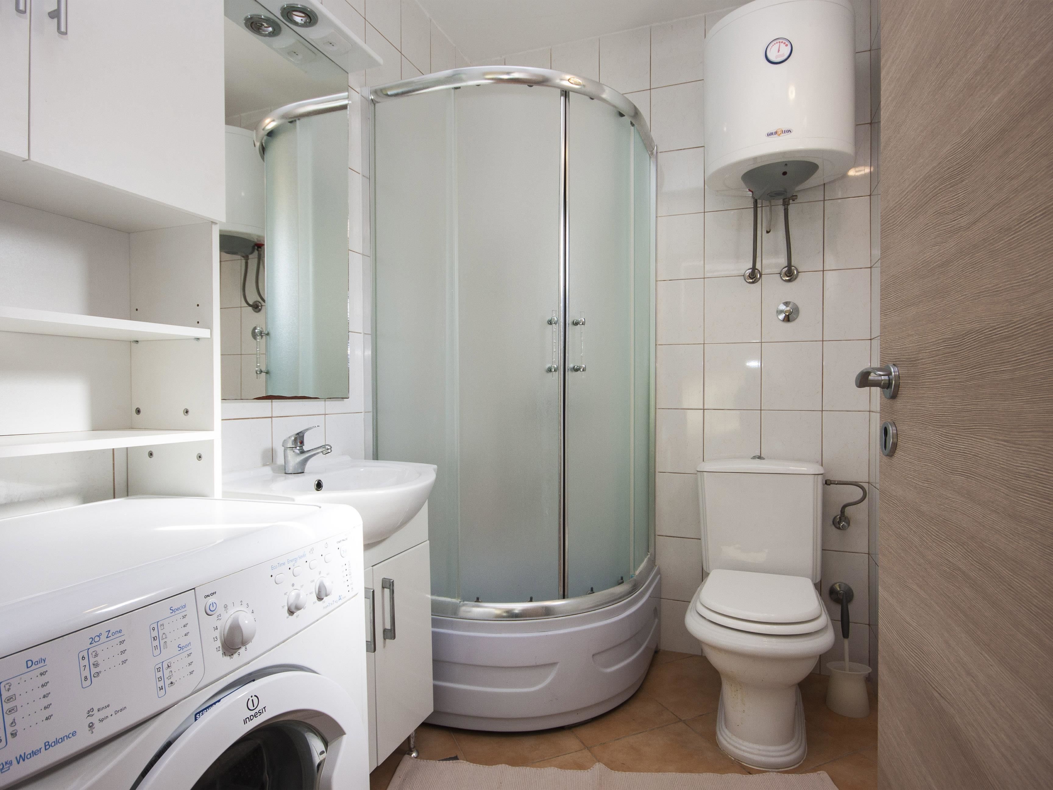 A modern bathroom with a glass-enclosed shower, a toilet, a sink, and a washing machine.