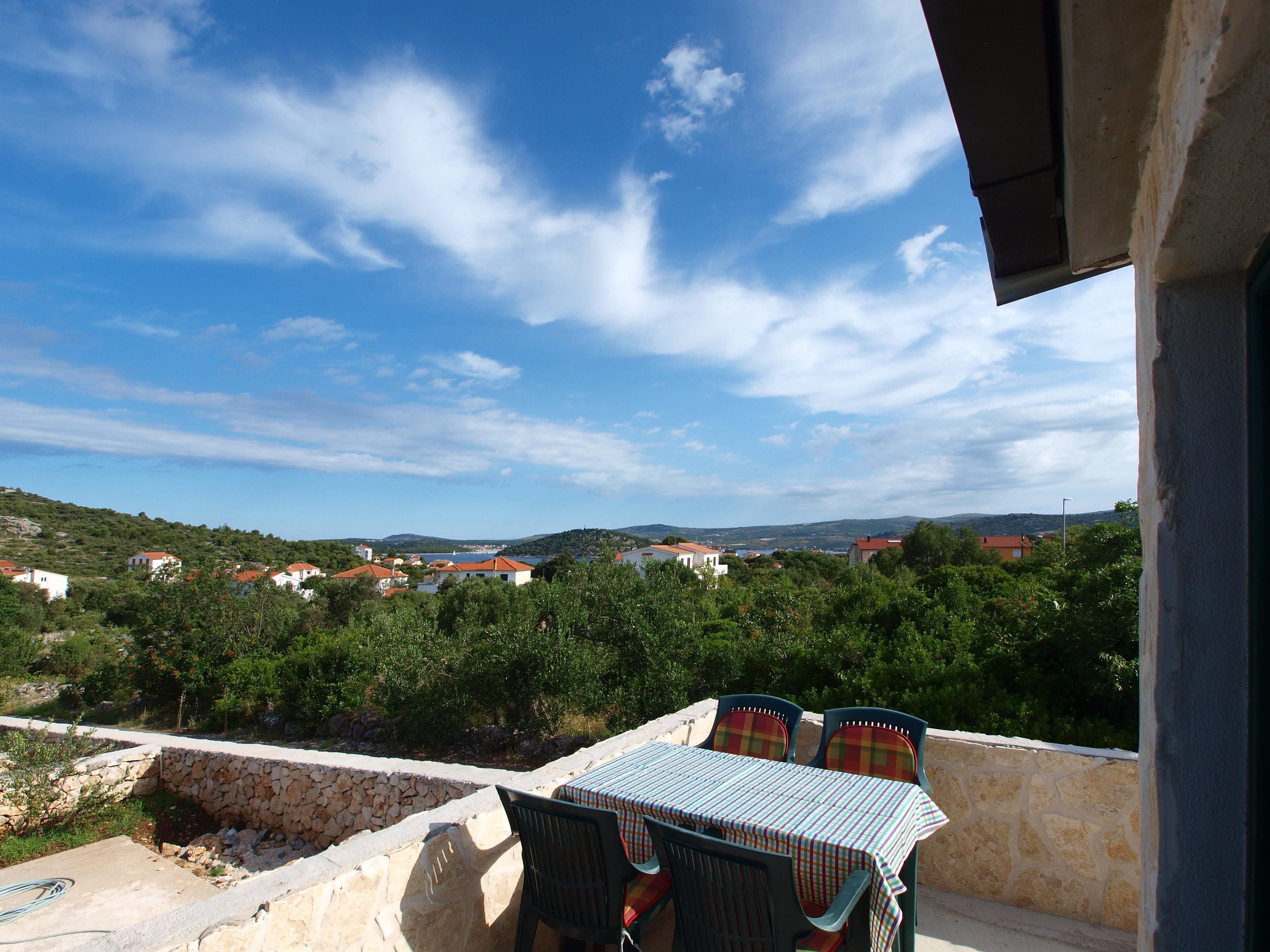 A terrace with a table and chairs, overlooking a scenic landscape with houses and hills.
