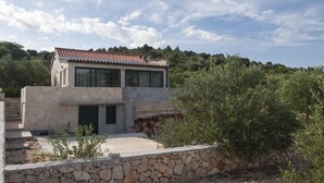 Ein modernes, zweistöckiges Haus mit Steinverkleidung und Ziegeldach, umgeben von Olivenbäumen und einer Steinmauer.