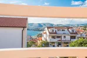 A coastal town with terracotta-roofed buildings, a view of the sea, and mountains in the background.