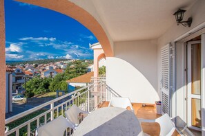 A balcony with a view of a town, white chairs, and a table.