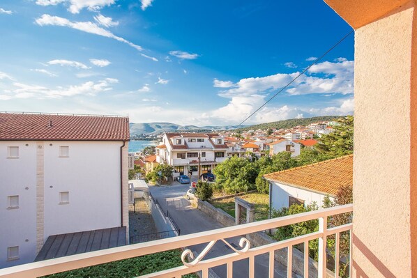 A balcony overlooking a coastal town with terracotta-roofed buildings, a clear sky, and a view of the sea.