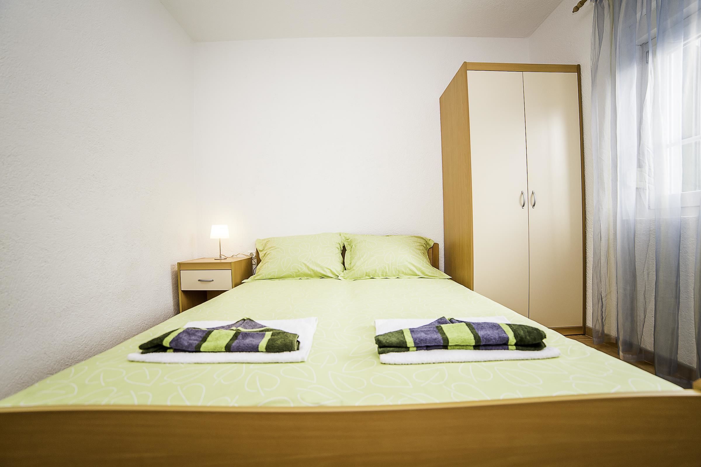 A neatly made bed with green bedding and two towels, a bedside table with a lamp, and a wardrobe with a mirror.