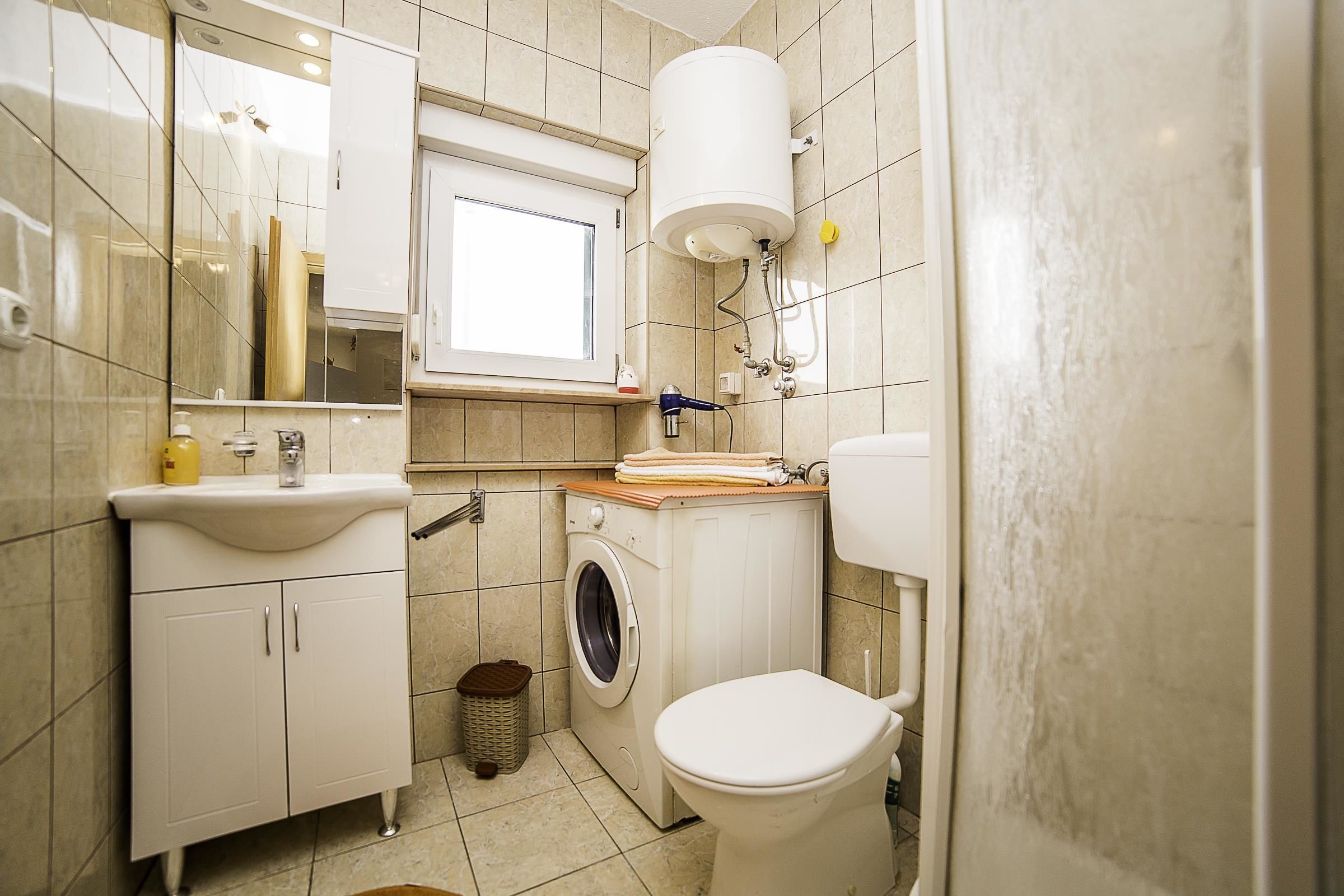 A compact bathroom with a sink, washing machine, toilet, and a window.
