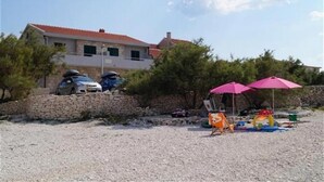 Un bâtiment avec un mur en pierre et des voitures garées. On aperçoit des parasols et des chaises de plage sur la plage.