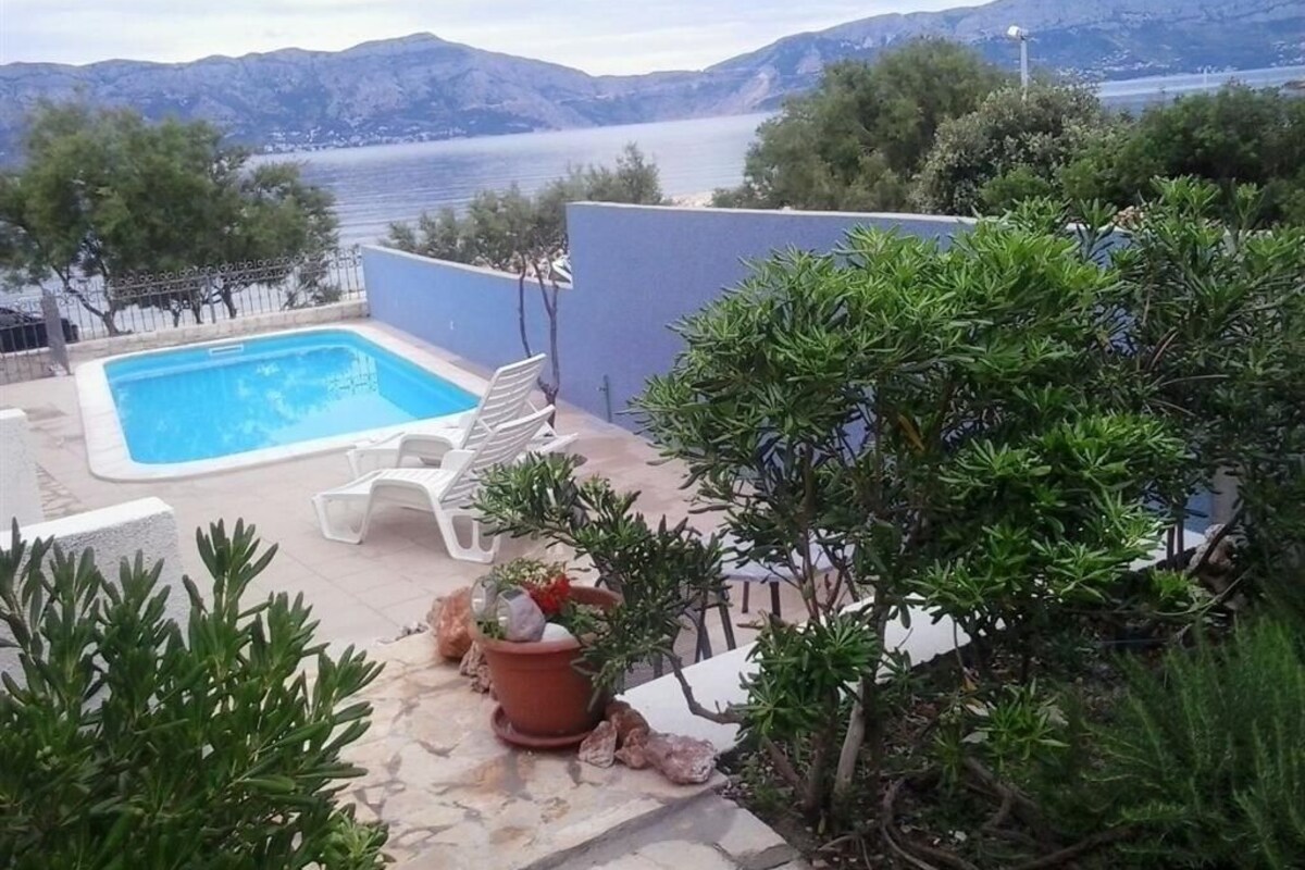 Une piscine entourée de chaises longues, agrémentée de plantes en pot et offrant une vue sur la mer et les montagnes.