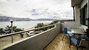Un balcon offrant une vue sur un lac et des montagnes, avec un espace salon extérieur et un scooter garé.