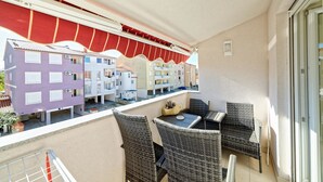 A balcony with wicker furniture and a red awning, overlooking a row of colorful apartment buildings.