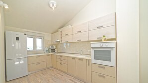 A modern kitchen with light wood cabinets, a stainless steel refrigerator, a microwave, and a built-in oven.