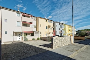 Une rangée d’immeubles résidentiels à plusieurs étages, dotés de balcons, un patio pavé et un ciel dégagé.