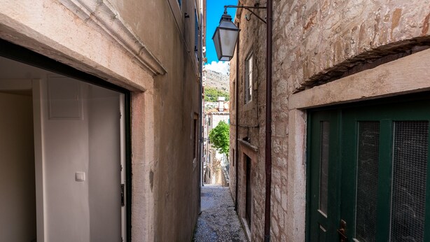 Un estrecho callejón con paredes de piedra, una puerta verde y una puerta blanca.