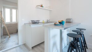Una cocina moderna con armarios blancos, una isla central con taburetes y un horno integrado.