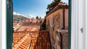 Vista desde un balcón con tejados de tejas de arcilla y un edificio de piedra con una ventana y una puerta.