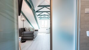 Una sala moderna con un sofá gris, una lámpara de pie y un ventanal con luz natural.