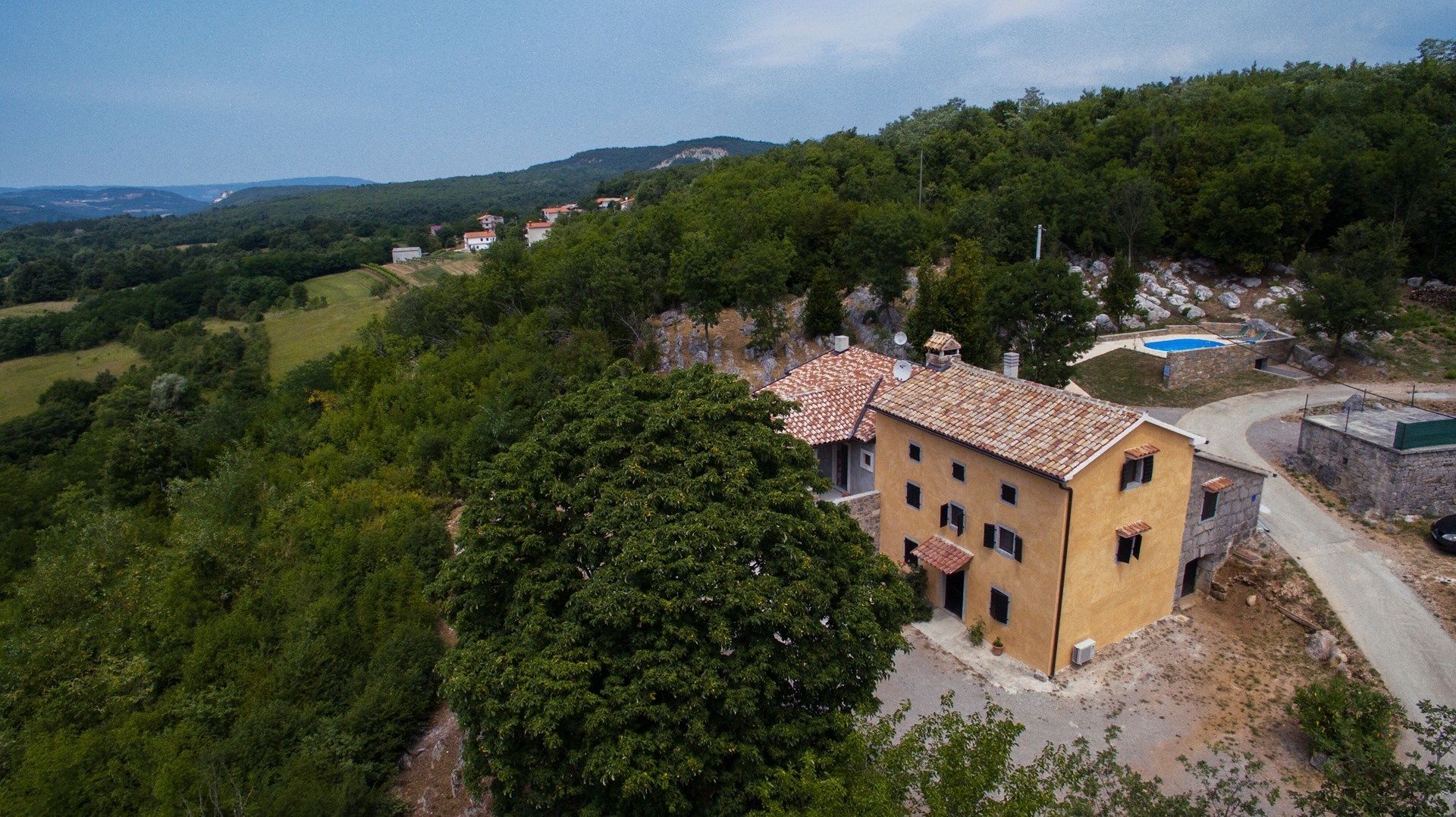 A two-story building with a tiled roof, surrounded by lush greenery and hills.