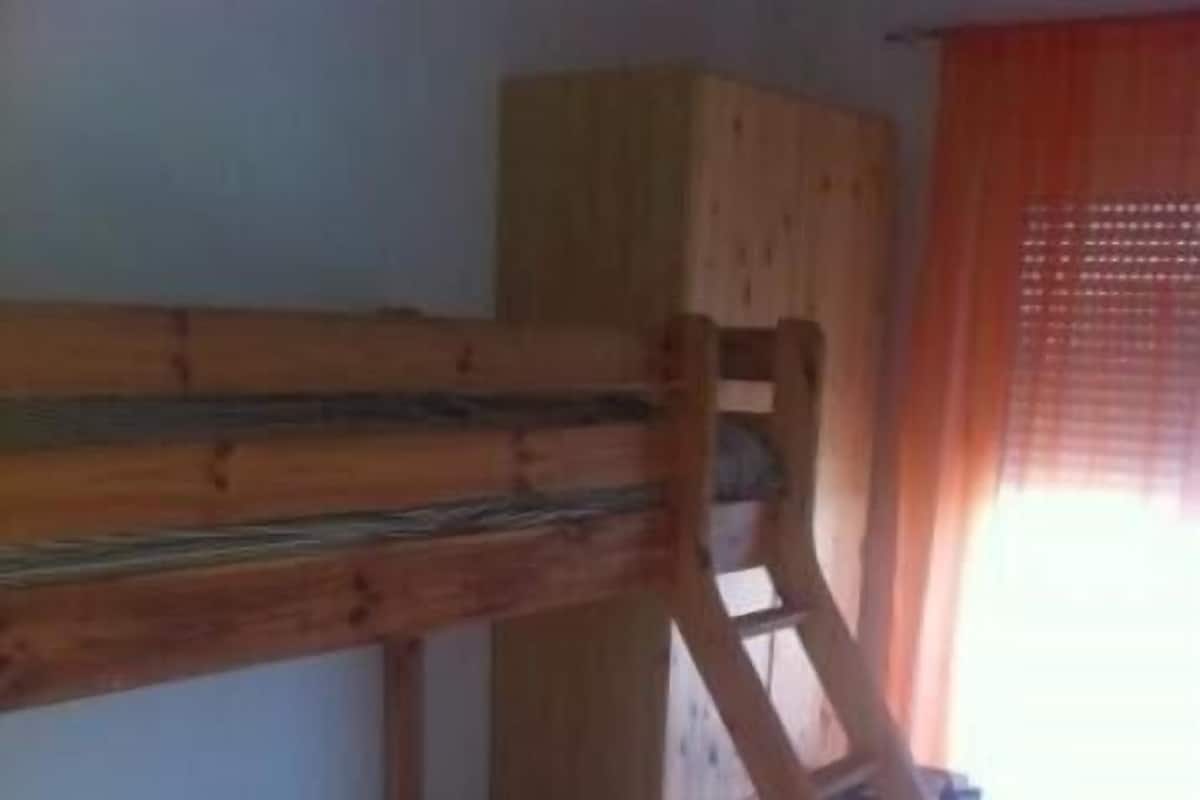Una cama litera con colchón y estructura de madera, un armario de madera y un suelo a cuadros.