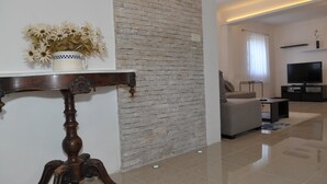 A modern living room with a brick accent wall, a wooden table with a vase of flowers, a grey sofa, a TV, and a coffee table. - Villa Sofija (Selca)