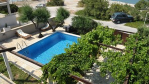 A swimming pool with a view of the sea, surrounded by greenery and a parked car. - Villa Sofija (Selca)