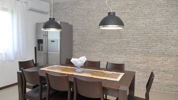 Comedor con pared de ladrillo, cocina moderna e iluminación colgante.