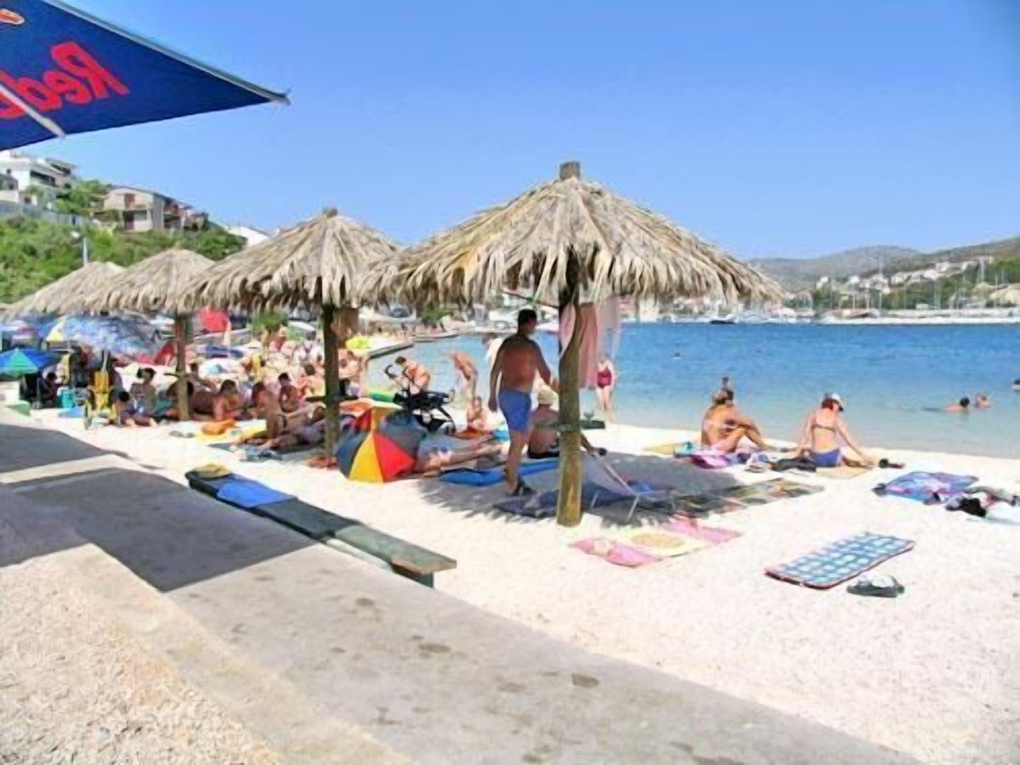 Una playa con sombrillas de paja, tumbonas y gente relajándose.