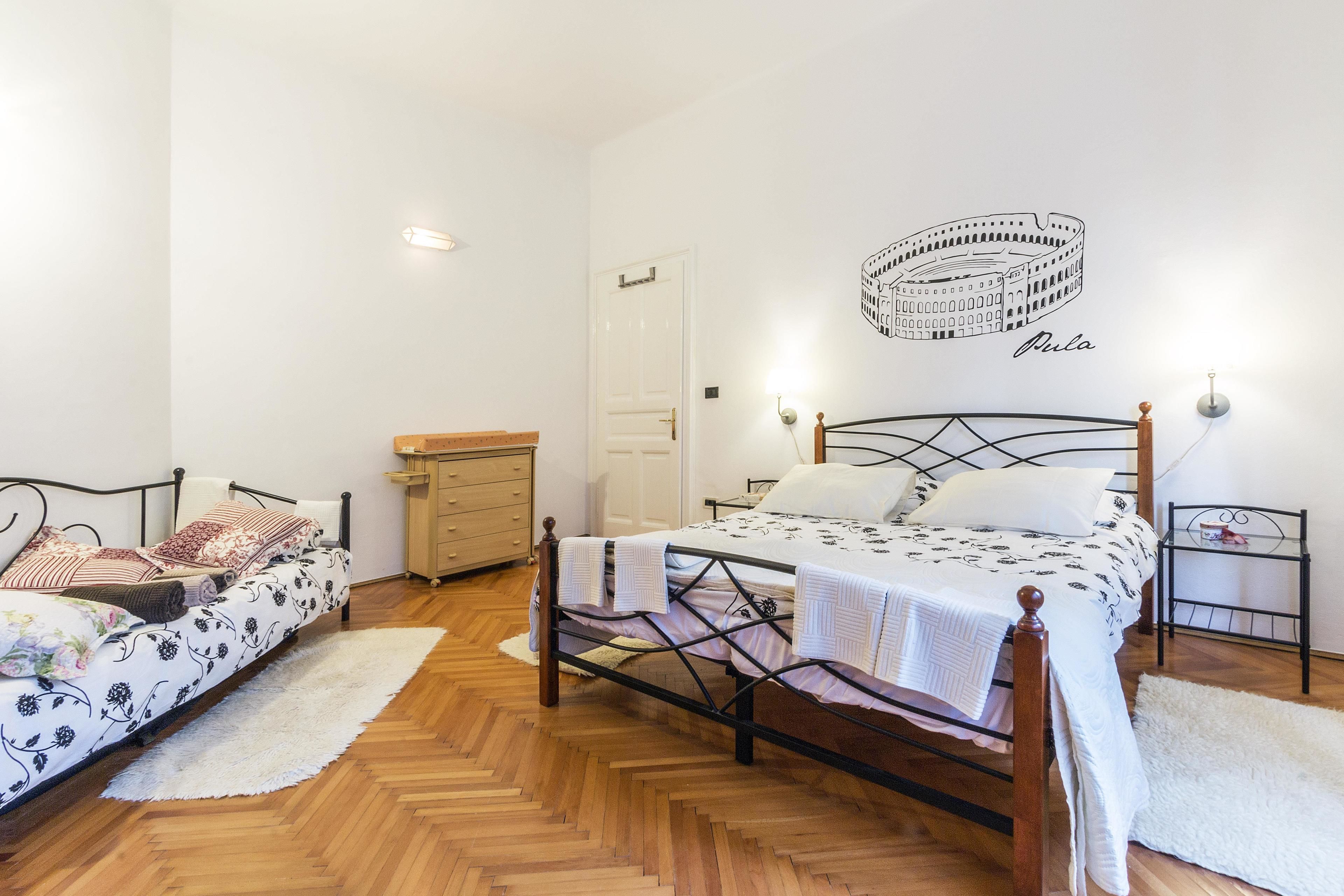 Une chambre avec deux lits, un plancher en bois, une porte blanche et un luminaire fixé au mur.