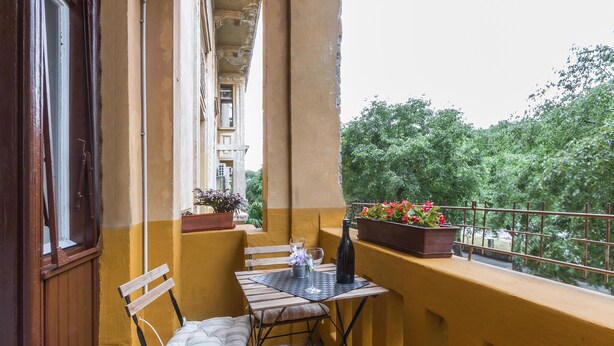 A balcony with a table, chairs, a potted plant, and a bottle.
