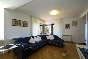 A modern living room with a dark blue sectional sofa, a small wooden table, and a radiator. - Apartment Gasparini / Three Bedrooms (Pula)