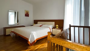 A hotel room with a wooden bed, a nightstand, a mirror, and a painting on the wall. - Apartment Gasparini / Three Bedrooms (Pula)