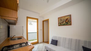 A compact living space with a kitchenette, a sofa, a painting, and a view through a door. - Apartments Grulović (Vodice)