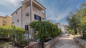 A two-story building with a balcony, a stone wall, and a narrow street. - Apartments Grulović (Vodice)
