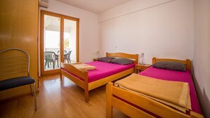 A room with two wooden beds, a chair, and a sliding glass door leading to an outdoor area with chairs. - Apartments Grulović (Vodice)