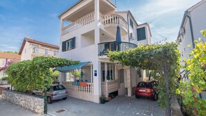 A two-story building with a balcony, a car parked in front, and a stone wall. - Apartments Grulović (Vodice)