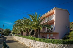 A pink building with a stone wall, a balcony, and palm trees.