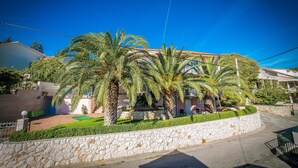 A residential building with a stone wall, palm trees, and a clear blue sky. - Apartments The Palms (Okrug)