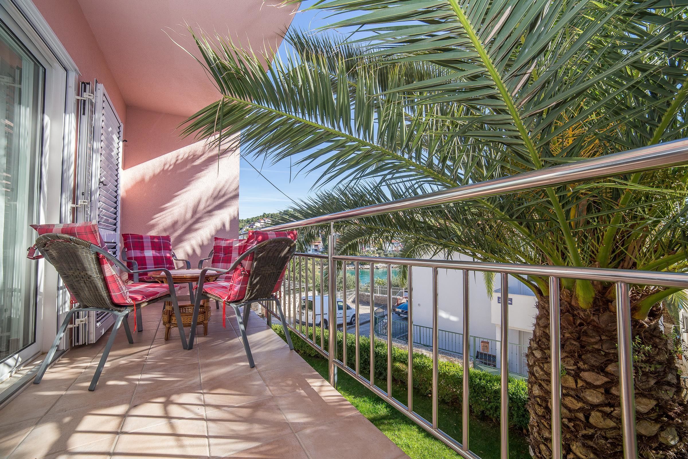 A balcony with a table and chairs, a palm tree, and a view of the street.