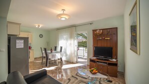 A living room with a sofa, TV, and a dining area with a table and chairs. - Apartments The Palms (Okrug)