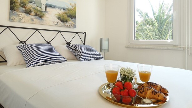 A neatly made bed with checkered pillows, a breakfast tray with strawberries and croissants, and a painting of a beach scene above the bed. - Holiday House Lidija (Medulin)