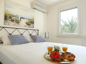 A neatly made bed with checkered pillows, a breakfast tray with strawberries and croissants, and a painting of a beach scene above the bed. - Holiday House Lidija (Medulin)