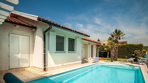 A swimming pool with a tiled deck, a covered patio area, and a few lounge chairs. - Holiday House Lidija (Medulin)