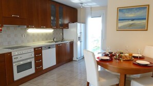 A modern kitchen with wooden cabinets, a built-in oven, and a dining area with a table set for two. - Holiday House Lidija (Medulin)